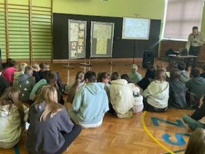 Uczniowie, zgromadzeni w sali gimnastycznej, słuchają prelekcji.