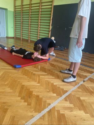 Uczeń pochyla się nad innym uczniem i sprawdza czy ten oddycha. 