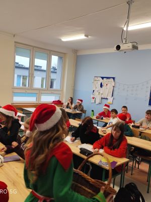 Uczniowie w świątecznych przebraniach rozdają mikołajkowe prezenty.