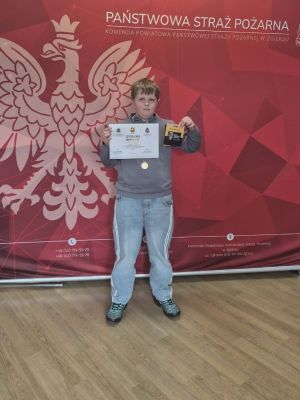 Tomasz dumnie pozuje z medalem, nagrodami oraz dyplomem za zdobycie I miejsca.