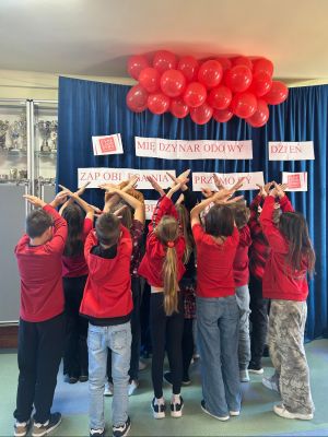 Uczniowie klasy 4a na tle plakatu informującym o Międzynarodowym Dniu Przeciwdziałania Przemocy wobec dzieci.