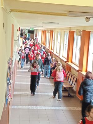 Uczniowie idą korytarzem szkolnym, wielu z nich ma na sobie czerwone elementy stroju związane z akcją tematyczną.