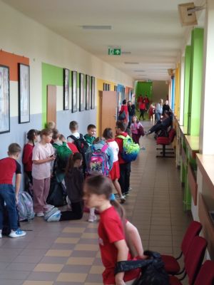 Na szkolnym korytarzu stoją i przechodzą uczniowie, z kt&oacute;rych wielu jest ubranych na czerwono w ramach akcji przeciw przemocy.